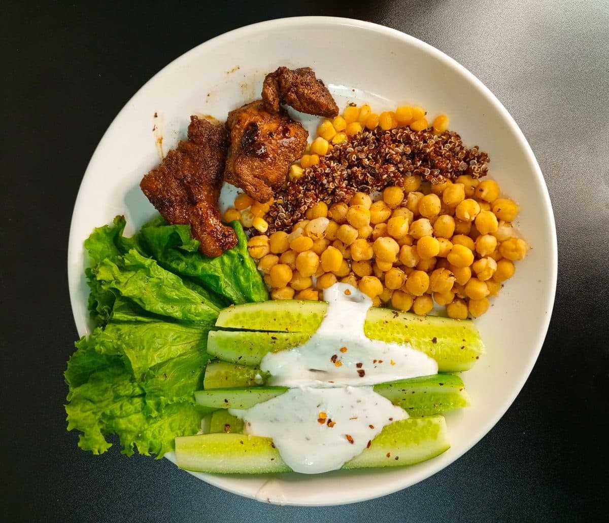 Prato equilibrado com folhas verdes, frango grelhado, grão de bico e legumes coloridos sobre mesa de madeira clara