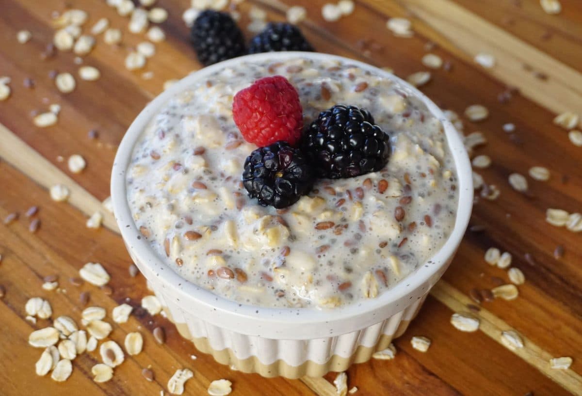 Tigela de aveia com frutas vermelhas, sementes de chia e um copo de água sobre mesa de madeira clara