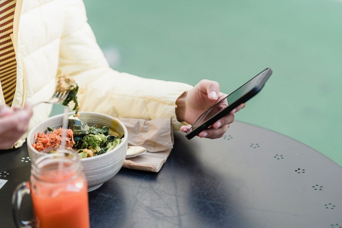 Mãos segurando um celular com o aplicativo do plano de saúde aberto ao lado de um recibo e uma salada colorida