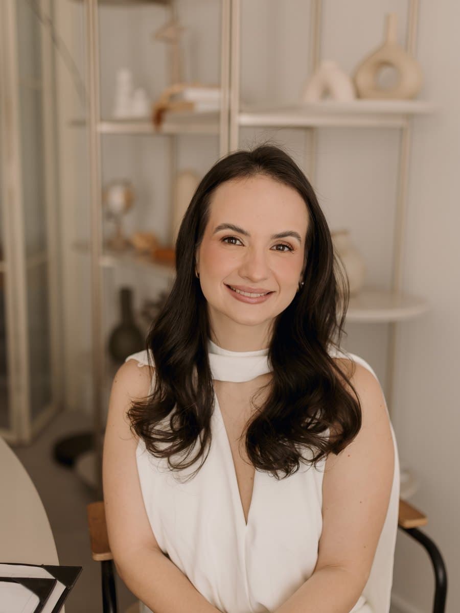 Beatriz Aires, nutricionista, de macacão branco, sentada e sorrindo